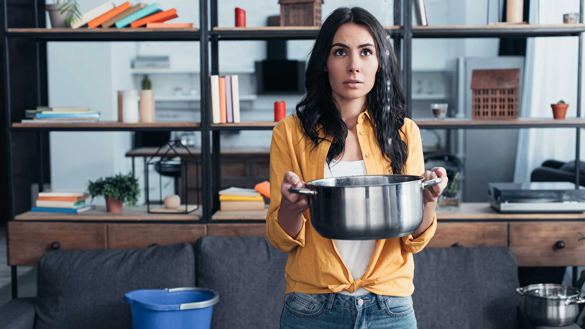Person holding a pot beneath a leak in a living room